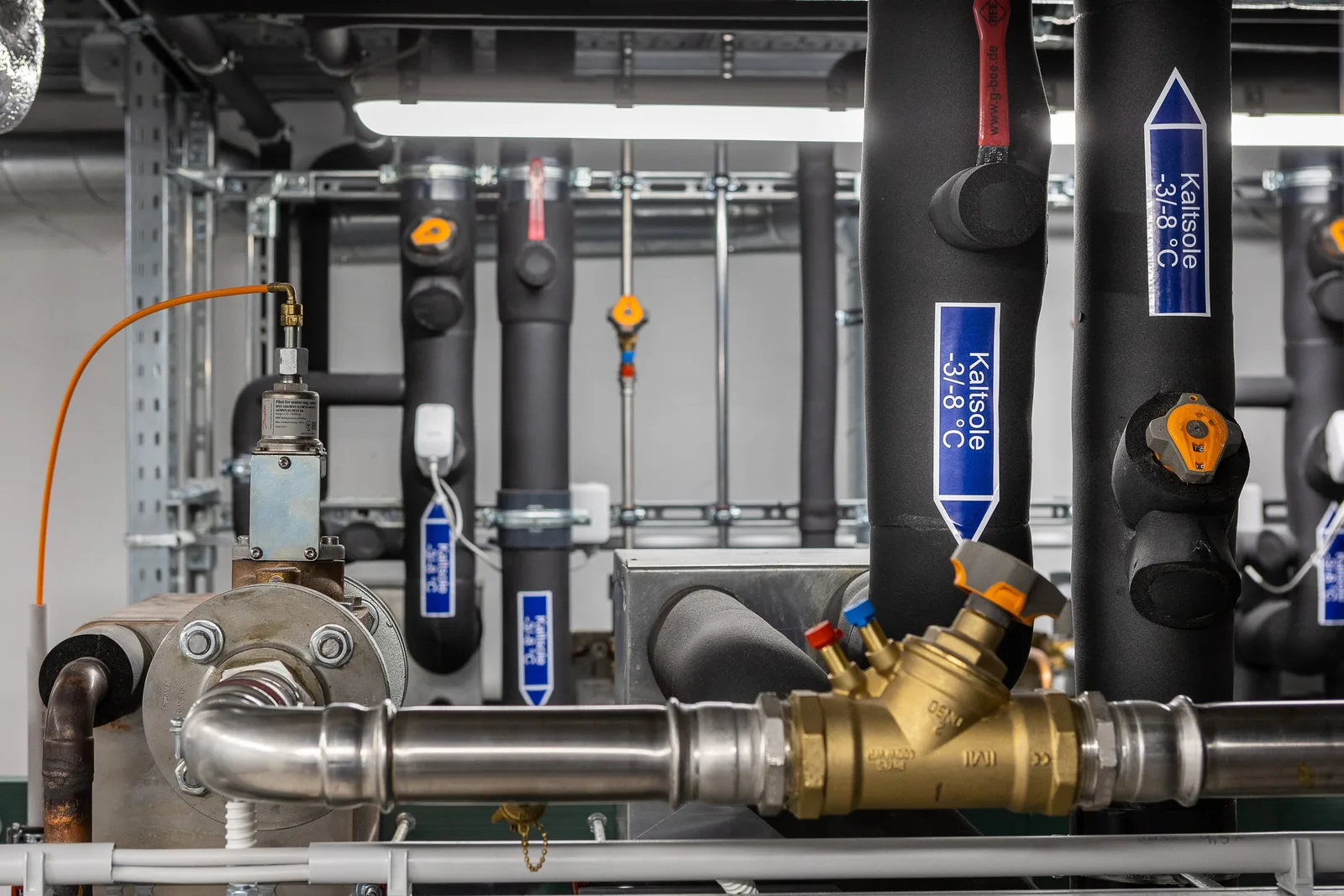 Rohrleitungen einer CO2-Kälteanlage mit blauen Beschriftungsetiketten und Messingventil