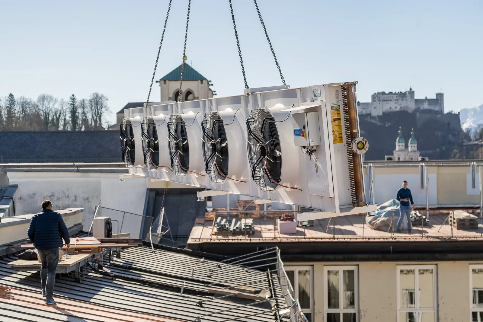 Ein Verflüssiger hängt am Kran über den Dächern von Salzburg, im Hintergrund die Festung